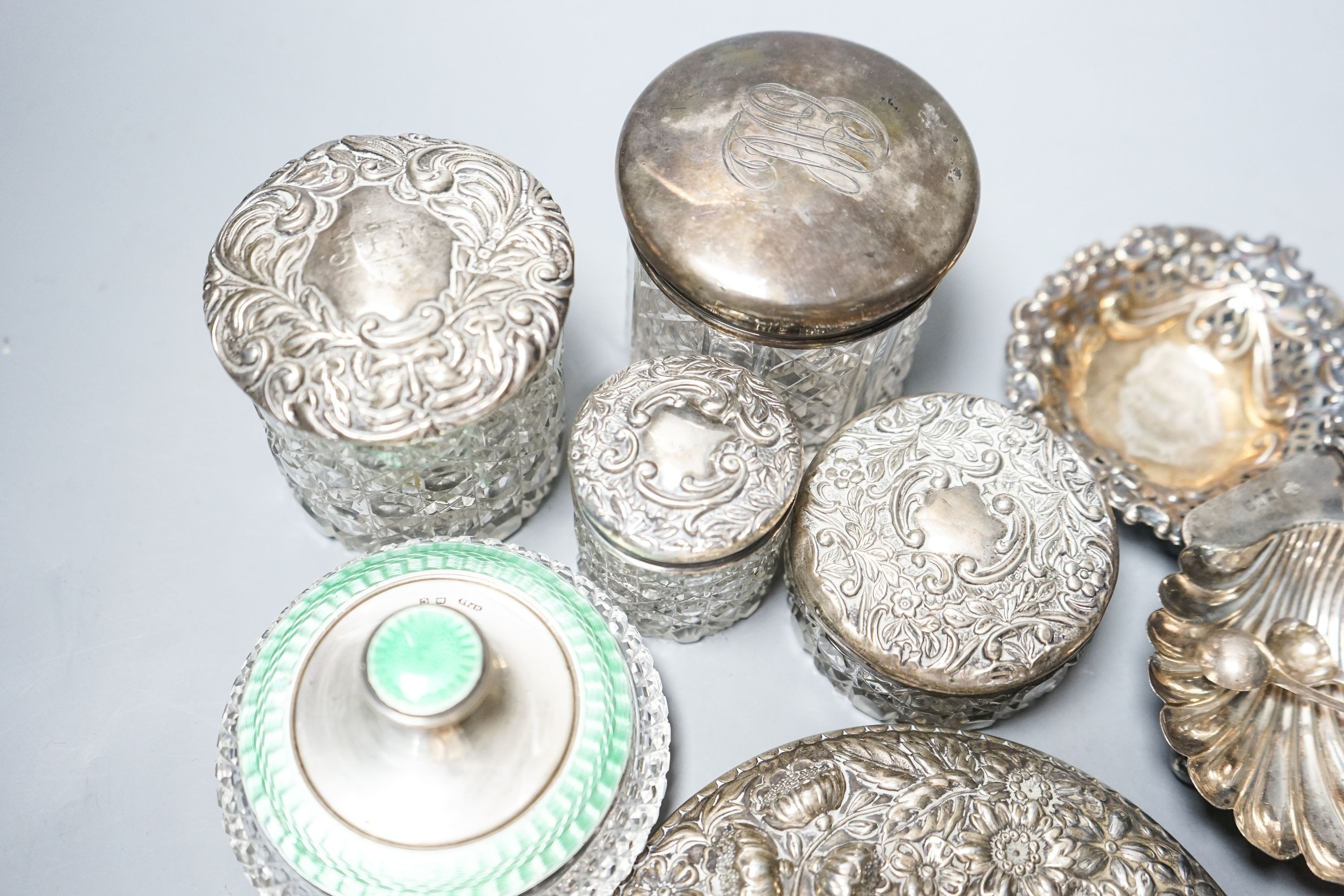 A silver and enamel mounted glass toilet jar, four other toilet jars, a hand mirror and three small silver dishes.